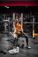 Fototapeta na wymiar Attractive slim fitness girl preparing gloves for starting exercising in the gym with equipment around her.
