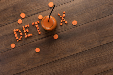 Inscription detox, carrot juice in a glass on a wooden background, top view. Concept of healthy eating, raw food diet, diet.