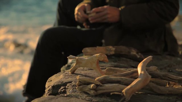 old man carving wood sculptures at seaside during sunset