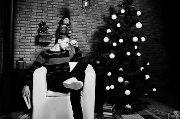 Naklejka na ściany i meble Studio portrait of man with book sitting on chair against christmass tree with decorations.