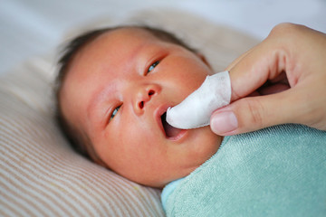 Mother use finger to clean baby tongue and gum with the clean gauze.