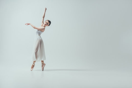 Fototapeta attractive ballerina in white dress dancing in studio, isolated on white