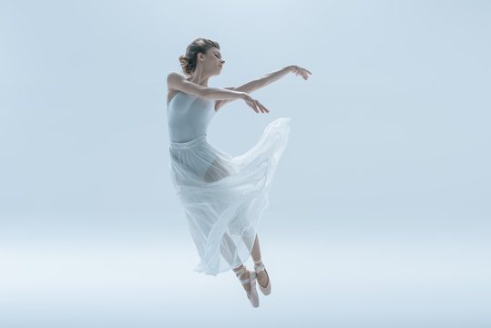 young ballerina in white dress jumping in studio, isolated on white