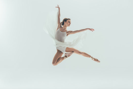 Fototapeta young elegant ballerina in white dress jumping in studio, isolated on white