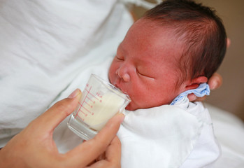 Mother feeding milk infant baby by glass cup.