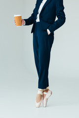cropped view of businesswoman in ballet shoes holding coffee to go, isolated on grey