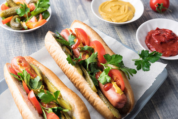 Hot dogs on wooden background. Homemade sandwiches with sausages, tomatos, pickles, mustard and ketchup on plate. Wrapping paper