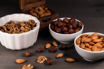 Two white cups filled with nuts, almonds, hazelnuts, walnut and a wooden casket with almonds