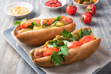 Hot dogs on wooden background. Homemade sandwiches with sausages, tomatos, pickles, mustard and ketchup on plate. Wrapping paper