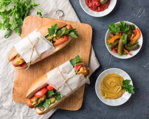 Hot dogs on wooden background. Homemade sandwiches with sausages, tomatos, pickles, mustard and ketchup on plate. Wrapping paper