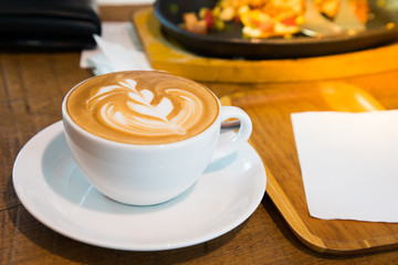 A cup of coffee late art in white cup and blur photo breakfast background o wood table