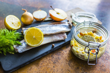 Prepared fresh salted herrings on a stone board and herrings salad in jar. 