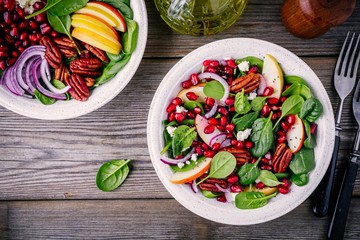 Homemade spinach, apple, pecan, red onion  salad with goat cheese and pomegranate on wooden background