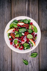 Homemade spinach, apple, pecan, red onion  salad with goat cheese and pomegranate on wooden background