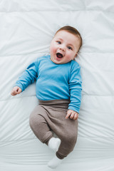 Portrait of an adorable 3 month old baby smiling lying in a bed of white sheets