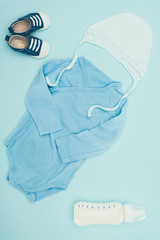 top view of baby clothes and bottle of milk isolated on blue