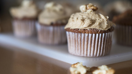Horizontal shot of coffee and walnuts homemade cupcakes with coffee icing, just taken out of the oven, positioned on a rustic white plastic board, indulgent dessert with considerable amount of sugar