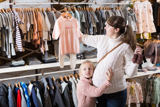 Pregnant female and small daughter choosing clothes