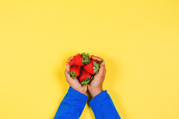 Kid hands holding fresh strawberries on yellow background