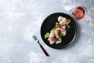 Foto op Plexiglas Vitello tonnato italian dish. Thin sliced veal with tuna sauce, capers and coriander served on black plate with fork and glass of rose wine over gray texture background. Top view, space © Natasha Breen