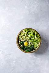 Obraz na płótnie Canvas Ceramic bowl with vegetarian green pea noodles with sliced cucumber, celery, spinach, quail egg yolk, pine nuts. Gray texture background. Top view, space. Healthy eating.