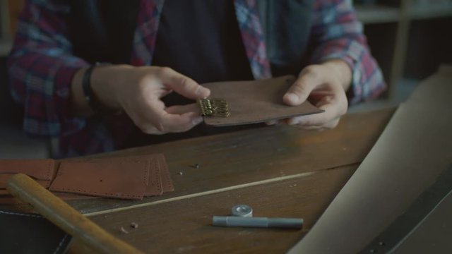 Craftsman making leather keychain in home workshop. Manufacture of leather goods in home workshop. Small workshop for manufacture leather goods