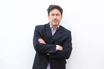 serious older businessman standing with arms crossed against white background