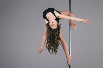upside down of beautiful female dancer in sportswear exercising with pole and looking at camera on...