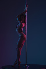 full length view of beautiful seductive young woman posing with pole on blue