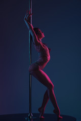 side view of seductive young female dancer leaning at pole on blue