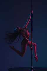 full length view of beautiful sensual young woman dancing with pole on blue
