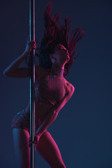 beautiful seductive young woman dancing with pole on blue