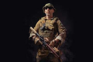 special forces soldier of the united states poses with a rifle on a black background