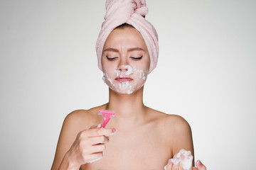 woman with a towel on her head performs facial hair removal with a razor