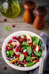 Homemade spinach, apple, pecan, red onion  salad with goat cheese and pomegranate on wooden background