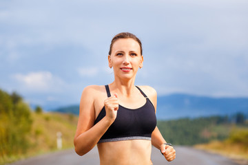 Young sporty woman jogging on mountain road. Running fitness girl in sportswear outdoor image with copy space