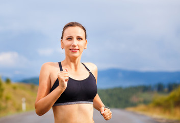 Young sporty woman jogging on mountain road. Running fitness girl in sportswear outdoor image with copy space