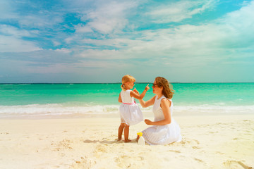 mother and daughter applying sunblock cream on beach