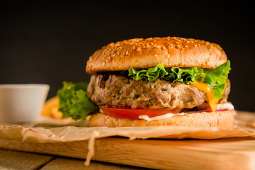 Classic burger with tasty beef, salad, sauce and tomato on dark background. American food