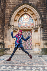 Happy traveler woman jumping at the cathedral with old gothic architecture