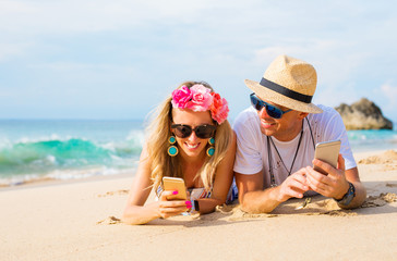 Couple lying on the beach and using mobile phones