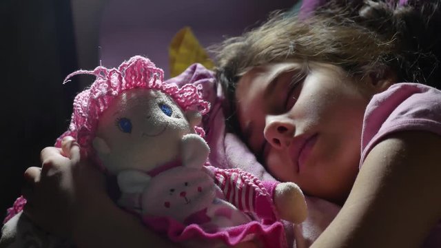 Adorable little girl night sleep in the sofa bed and hug her baby doll. girl brunette teenager cute indoors asleep on the bed