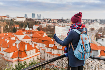 Young woman traveler with backpack looking at the map in old European town at winter holiday