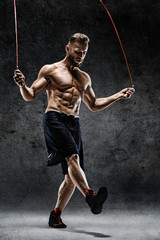 Best cardio workout. Young man skipping with a jump rope on dark background. Strength and motivation