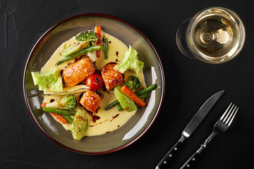 Fried piece of salmon with creamy sauce and green vegetables decorated with cherry tomato and slice of lemon