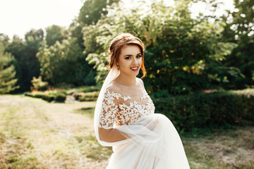 bride in a dress standing in a green garden and holding a wedding bouquet of flowers and greenery