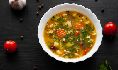 Bowl of chicken soup with noodle and vegetables on a dark wooden background.
