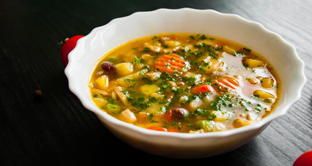 Bowl of chicken soup with noodle and vegetables on a dark wooden background.