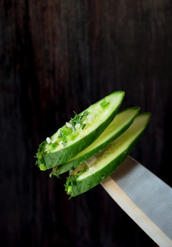 Slices of cucumber on a sharp knife on dark background