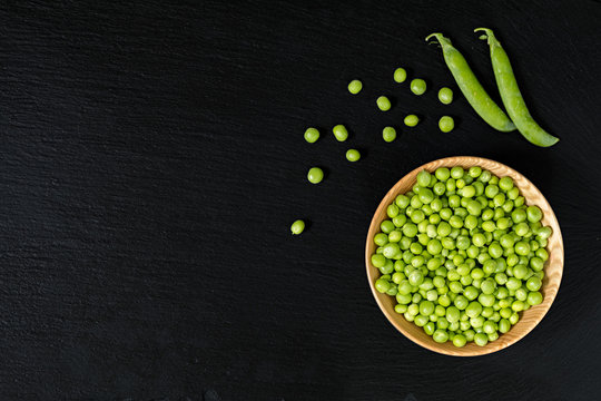 Grains fresh green peas in wooden bowl on a black stone surface.  Top view, copy space. Healthy eating concept.